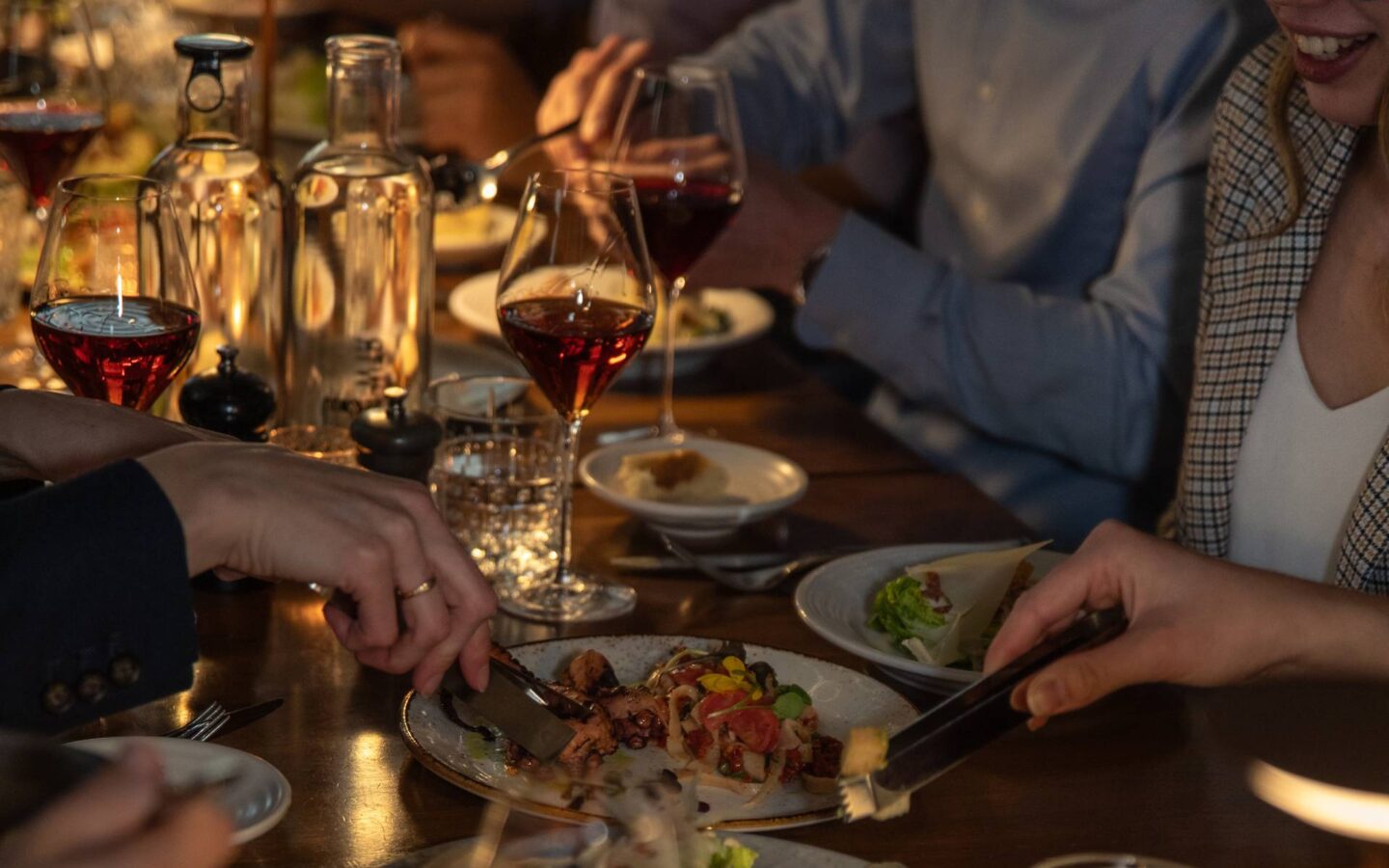 Guests enjoying a shared dinner with wine, appetizers, and candlelight in a warm, intimate restaurant setting.