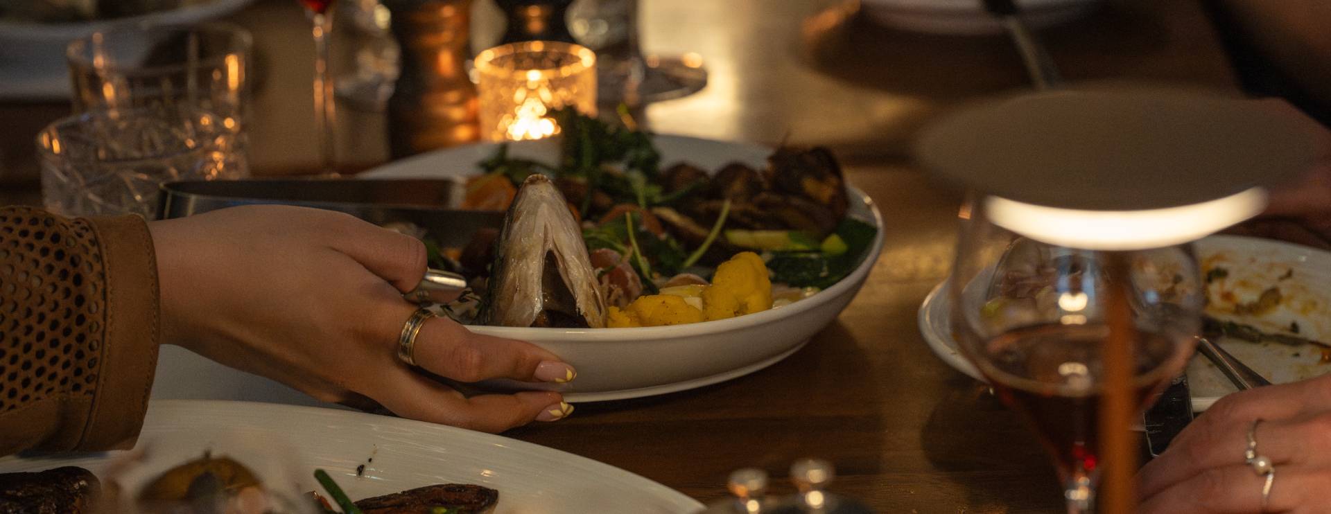 People sharing a seafood dish at a dimly lit restaurant table with wine glasses, candlelight, and a cozy dining atmosphere.